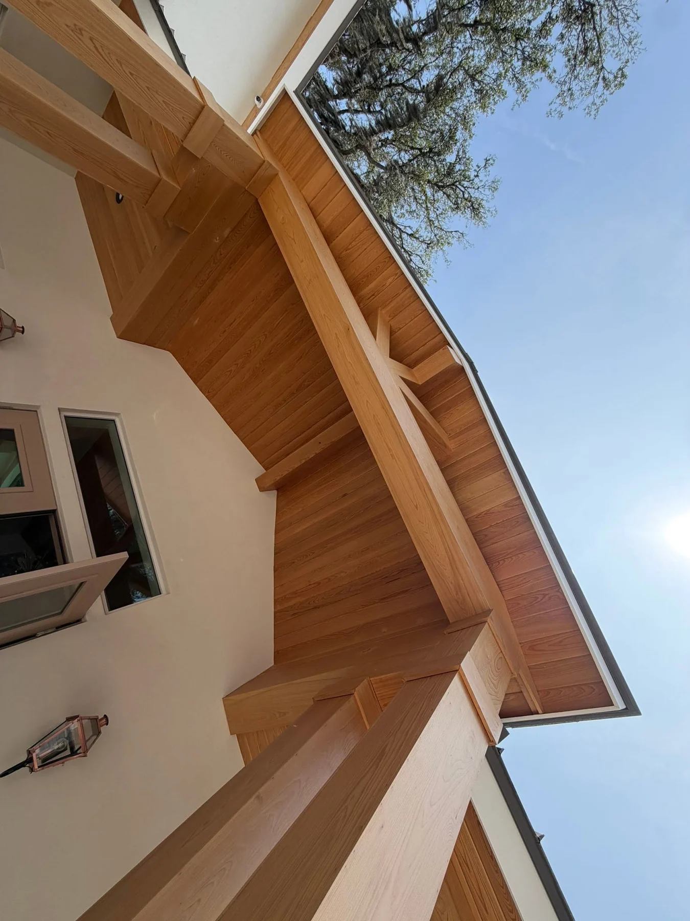 Detailed natural-wood exterior soffit, beams and column wraps against a blue sky