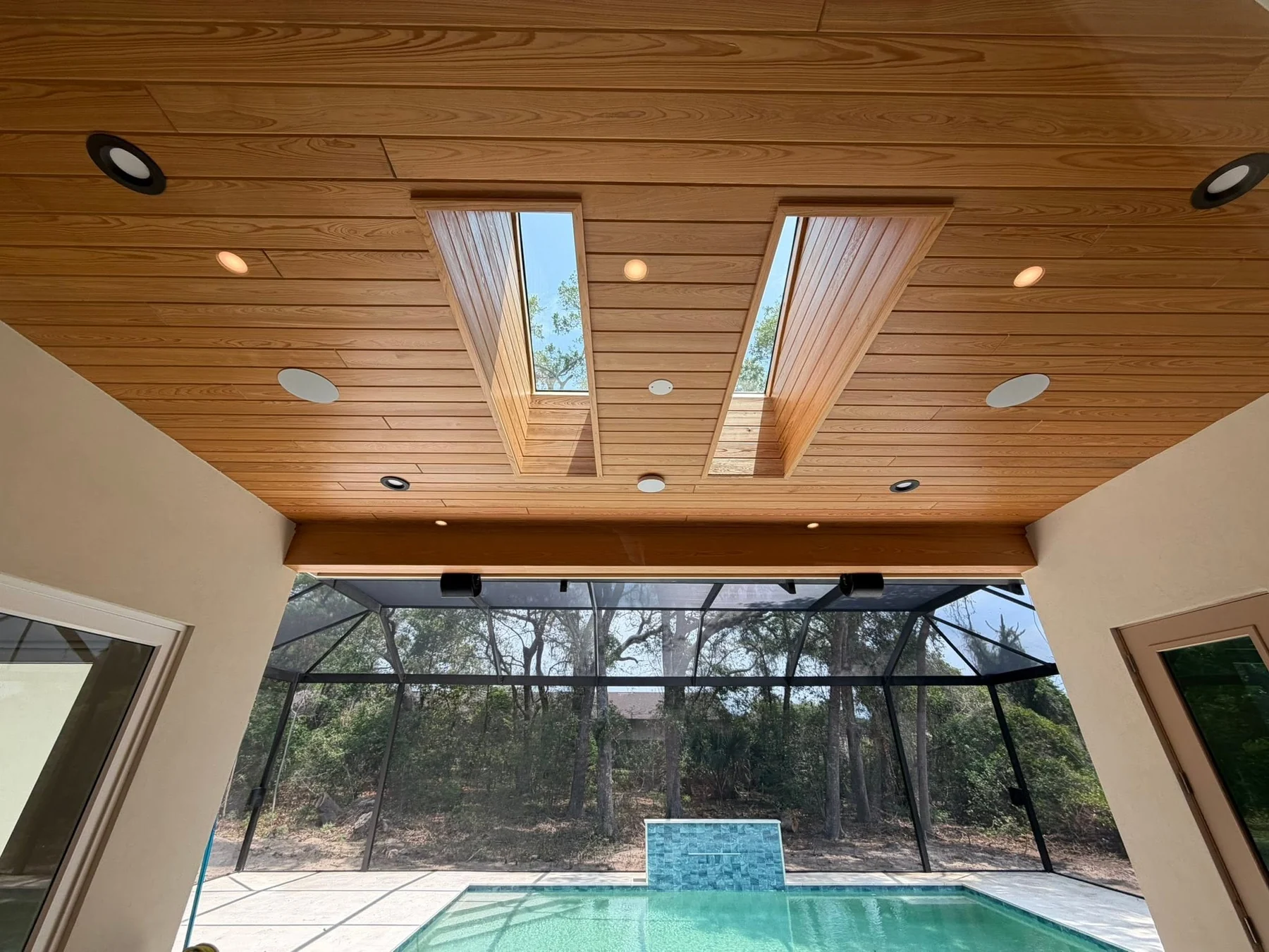 Finished natural-wood lanai ceiling with recessed lights and skylights above a pool